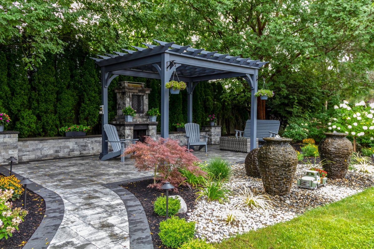 Modern backyard landscape with pergola, pavers, and outdoor fireplace